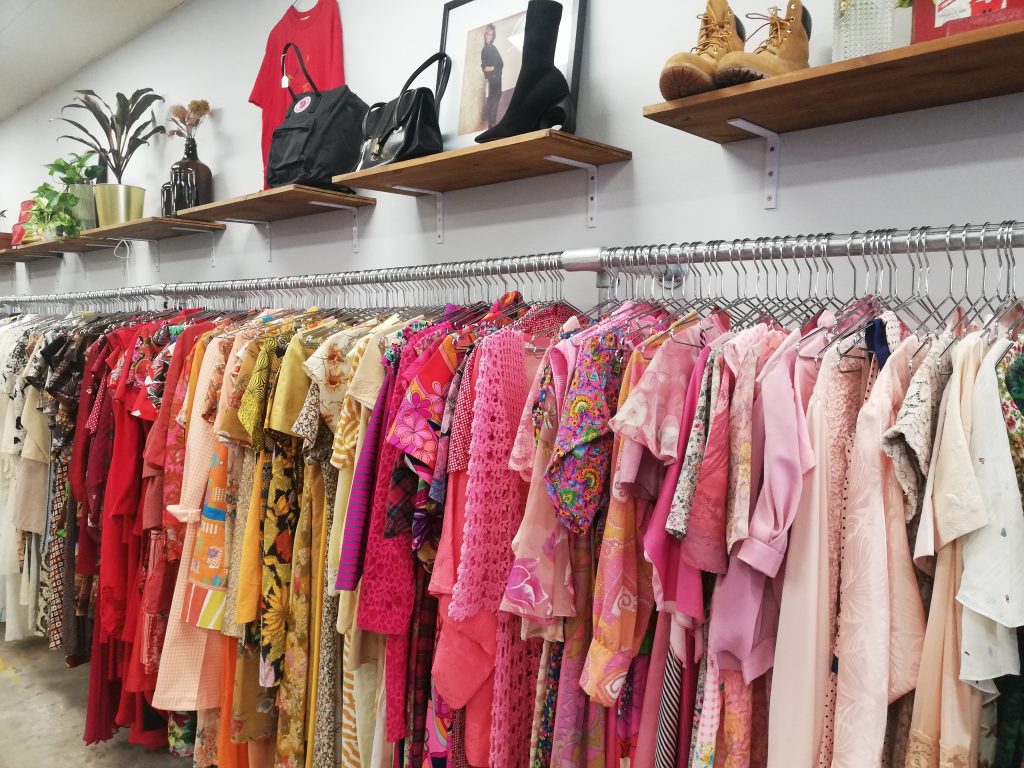 Row of colourful vintage dresses in a shop, with shoes on rack above