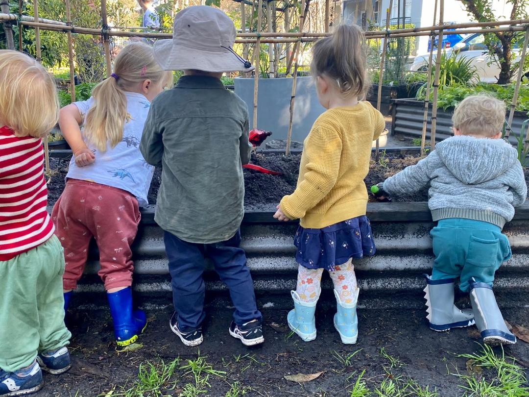 Small children standing at a raised garden bed, seen form behind
